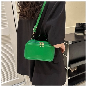 Detail view of grass green crossbody bag showing double gold zippers and leather handle