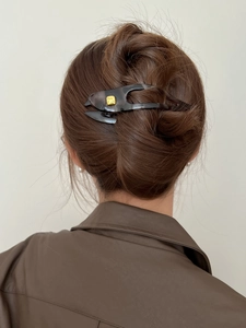 Detail view of large dark grey translucent hair clip with golden fashion logo on hair