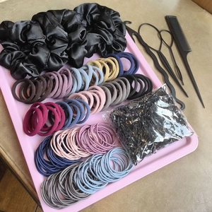 Macro shot of assorted silk scrunchies and hair styling tools on a pink tray