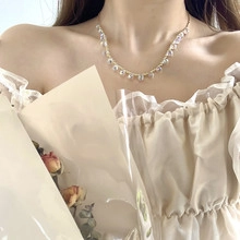 Detail shot of a minimalist gold snake chain necklace with a clear teardrop charm on a model