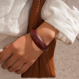 Close-up of a wide vintage dark red acrylic bangle worn on a wrist with neutral outfits
