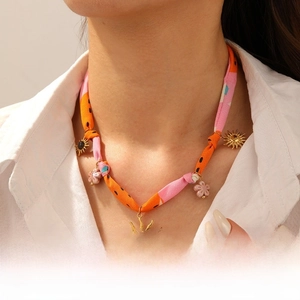 Détail du collier style soie avec lien en tissu orange et pendentifs soleil dorés