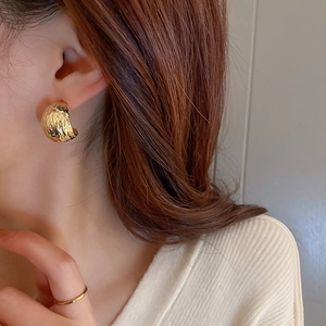 Macro view of gold C-shape stud earrings with hammer texture and pleated metal design