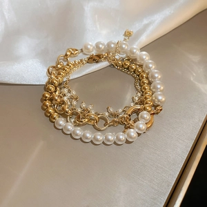 Detail of layered gold bead and pearl bracelets with vintage metal toggle clasp
