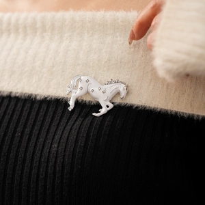 Detail of vintage white enamel horse brooch with sparkling rhinestones on fabric