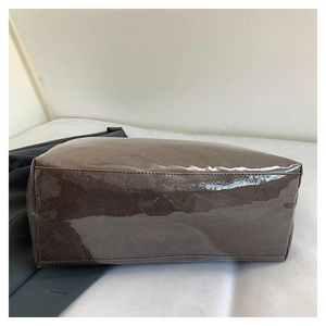 Detailed base and corner view of a brown glossy patent leather tote bag with stitching