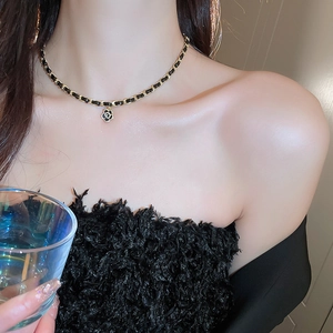 Detail of camellia flower pendant on woven gold chain and black leather necklace