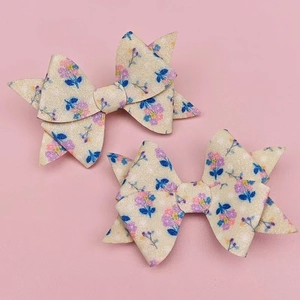 Detail view of two sequined bow hair clips with glitter floral print on pink background