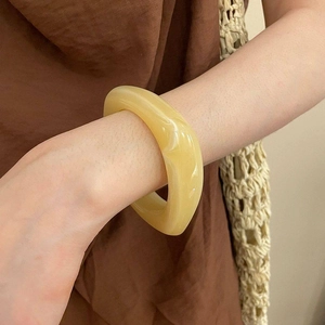 Makro-Detail des klobigen cremefarbenen Acryl-Armreifs mit Marmorstruktur am Handgelenk