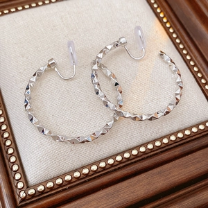 Close-up of silver geometric C-shaped clip-on earrings with textured metal surface