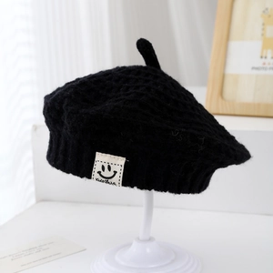 Dettaglio di un berretto in maglia nera per bambini con toppa a sorriso e punta superiore
