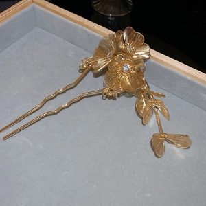 Close-up of golden flower hair stick with rhinestone centers and elegant leaf tassels