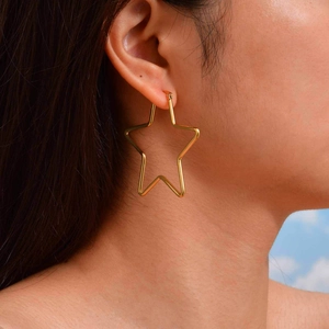 Side view of large hollow star-shaped gold earrings worn by a model against blue sky