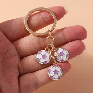 Detail of three purple soccer ball charms on a golden keychain held against pink background