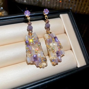 Close-up of geometric square earrings with purple crystals and gold metal edges in box