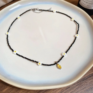 Detail of black beaded necklace with daisies and yellow marquise pendant on blue tray