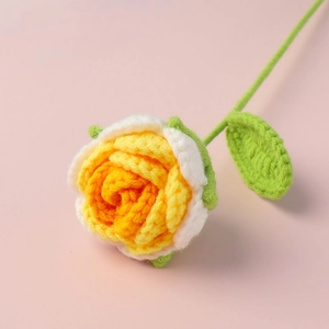 Detail of handmade crocheted rose in yellow and white gradient with green leaves
