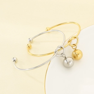 Detail of gold and silver knotted bangles with hollow steel ball charms on layered background