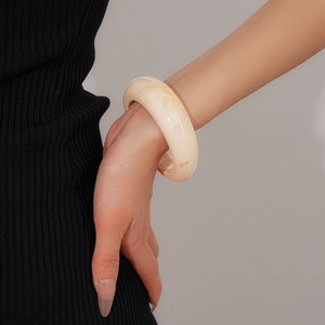 Close-up of a wide marbled resin bangle in cream white on a model's wrist