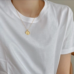 Detail of a gold coin pendant necklace with embossed figure on a thin cross chain