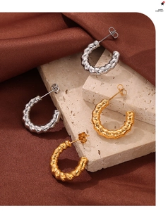 Detailed close-up of C-shaped spiral gold and silver hoop earrings on stone