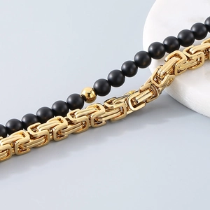 Detail of golden Byzantine chain paired with black matte beaded bracelet on marble
