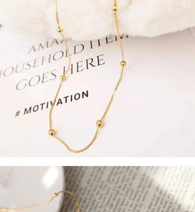 Macro detail of 18K gold bead snake chain necklace on minimalist white background