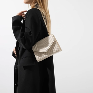 Elegant cream quilted leather shoulder bag with gold chain strap on a black blazer