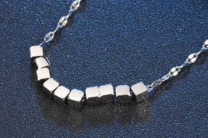 Macro view of silver titanium steel necklace with minimalist cube pendants on a blue background
