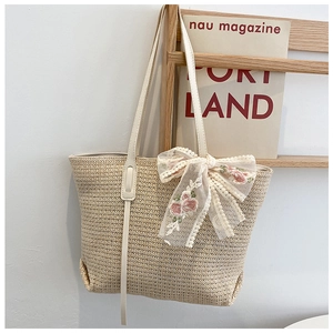 Detail of cream straw tote bag featuring pink floral lace bow embroidery on a wooden rack