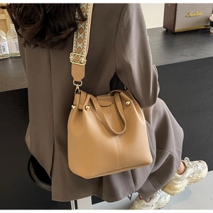 Detail of beige lychee leather bucket bag with geometric wide strap and gold hardware