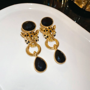 Macro shot of gold leopard head earrings with drop-shaped black gemstones on white ceramic