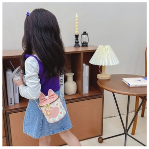 Detail of pink cylinder kids crossbody bag with heart pattern and oversized bow