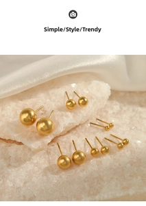 Macro detail of various sized gold ball stud earrings arranged on white stones and silk fabric