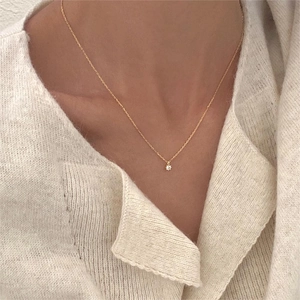 Close-up of a minimalist gold necklace with a single zircon pendant on a model's neck