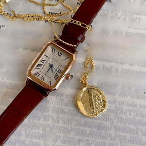 Elegant gold square watch and irregular lava pendant necklace on vintage paper