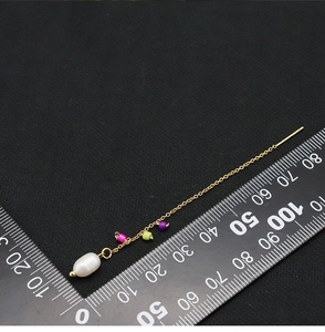 Macro detail of long gold pearl earring with colorful beads next to a measurement ruler
