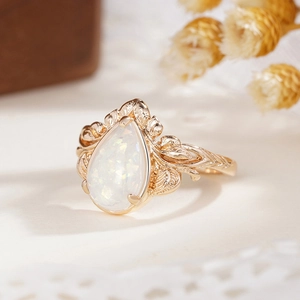 Macro detail of leaf textured gold ring featuring a pear cut white opal stone
