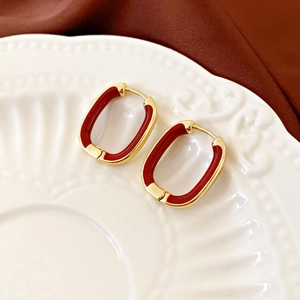 Detail of red and gold oval geometric hoop earrings on a vintage textured porcelain plate