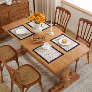 Macro view of four cotton linen placemats with blue diamond patterns on a wooden dining table