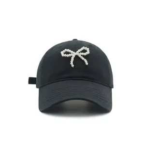 Detail view of a black cotton baseball cap featuring a white pearl bow decoration on the front