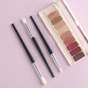Flat lay of 10-color eyeshadow palette with 3 makeup brushes on soft pink backdrop