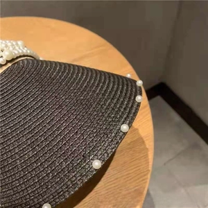 Detail of dark brown straw sun hat with elegant pearl embellishments on woven texture