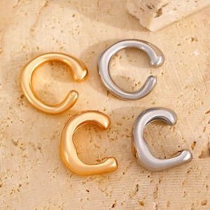 Dettaglio di ear cuff irregolari oro e argento posati su una pietra naturale beige