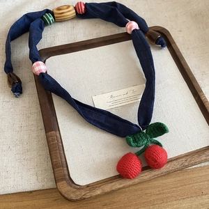 Close-up of handmade crochet red cherry pendant with wooden beads on navy fabric cord