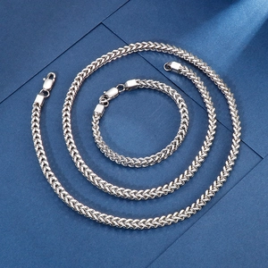 Vue détaillée du collier et du bracelet en maille épi en acier inoxydable argenté sur fond bleu