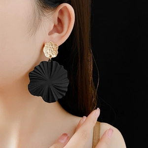 Close-up of elegant gold textured and black floral drop earrings worn by a model