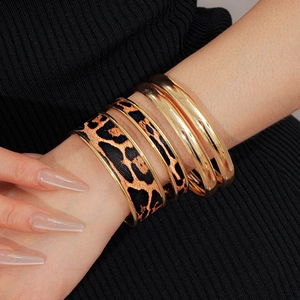 Gros plan de bracelets joncs dorés et imprimé léopard superposés sur le poignet
