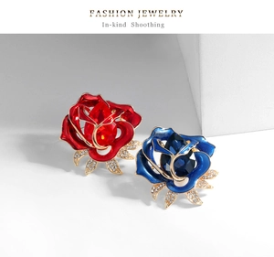 Detailed close-up of red and blue enamel rose brooches with teardrop crystal and gold finish