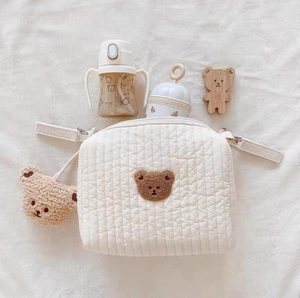 Close-up of beige quilted cotton diaper bag featuring cute bear embroidery and charm